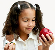 A young girl tries to decide between a candy bar and an apple. - Copyright – Stock Photo / Register Mark