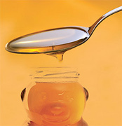 A spoon pouring honey into a bottle shaped like a bear. - Copyright – Stock Photo / Register Mark
