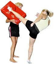A female kickboxer performing a high kick into a training bag held by a female trainer. - Copyright – Stock Photo / Register Mark