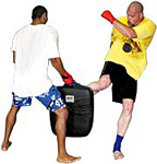 A training kickboxer performs knee-kick into a practice bag held by his sparring partner. - Copyright – Stock Photo / Register Mark