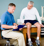 A middle aged man sits on an examining table next to a seated doctor. - Copyright – Stock Photo / Register Mark