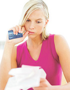 Woman with credit card in hand studies some sales receipts. - Copyright – Stock Photo / Register Mark