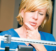 A middle aged woman contemplating the results of the scale she is standing on. - Copyright – Stock Photo / Register Mark
