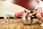 A woman does chest excercises on a workout ball while being spotted by her partner. - Copyright – Stock Photo / Register Mark