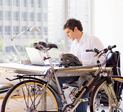 A young man at work with his bicycle leaning against his desk. - Copyright – Stock Photo / Register Mark